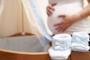 Zwanger vrouw naast een wieg met babyshoentjes